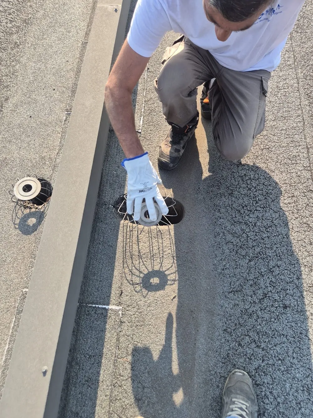 Technicien dégageant une évacuation d’eaux pluviales sur une toiture-terrasse