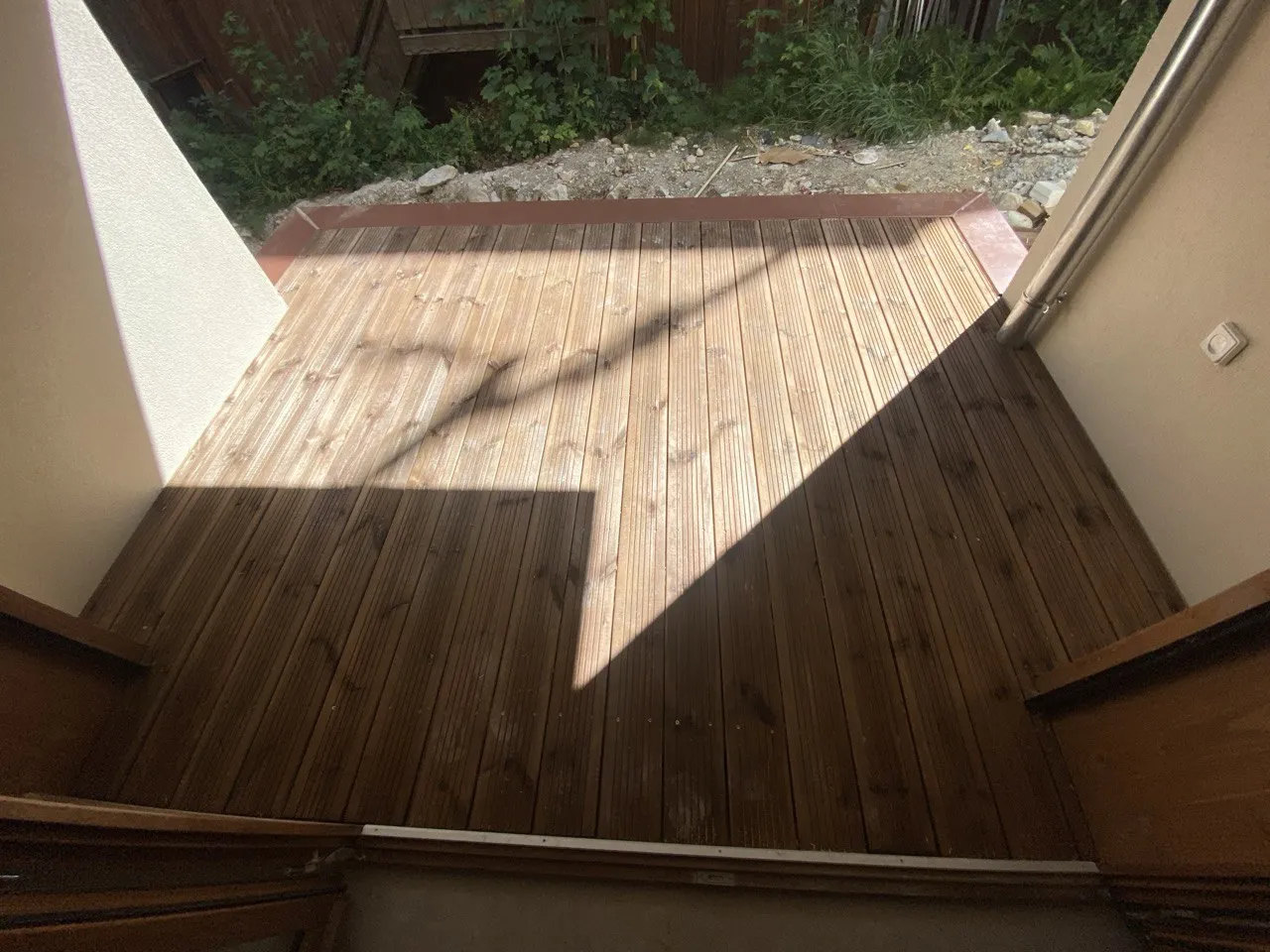 Terrasse en lames de bois posée entre deux murs de maison